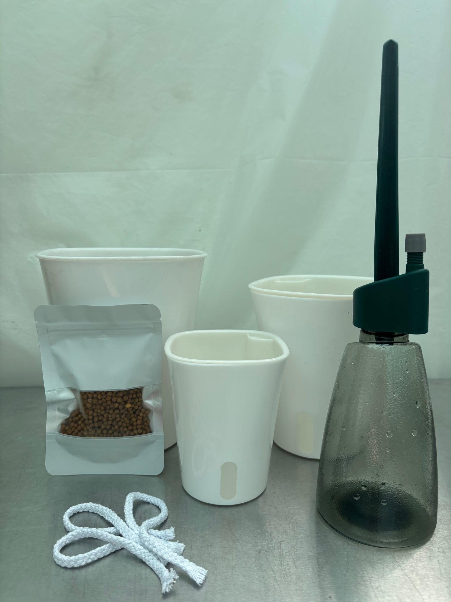 Lazy plant parent bundle with self-watering pots, water level indicator bottle, LECA clay pebbles, and wicking cords for low-maintenance plant care.